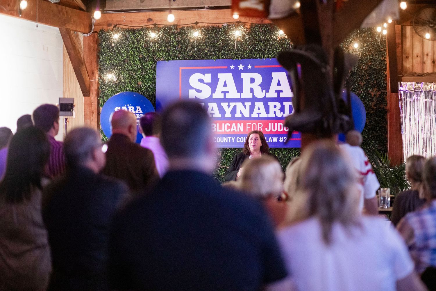 Political campaign rally showing stage lighting and crowd gathering indoors at an evening event.