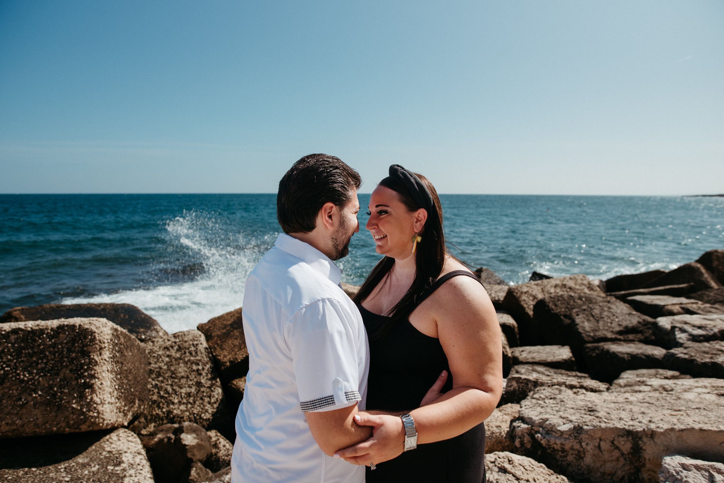 Couple shares intimate moments on rocky coastal cliffs with ocean waves crashing in background.