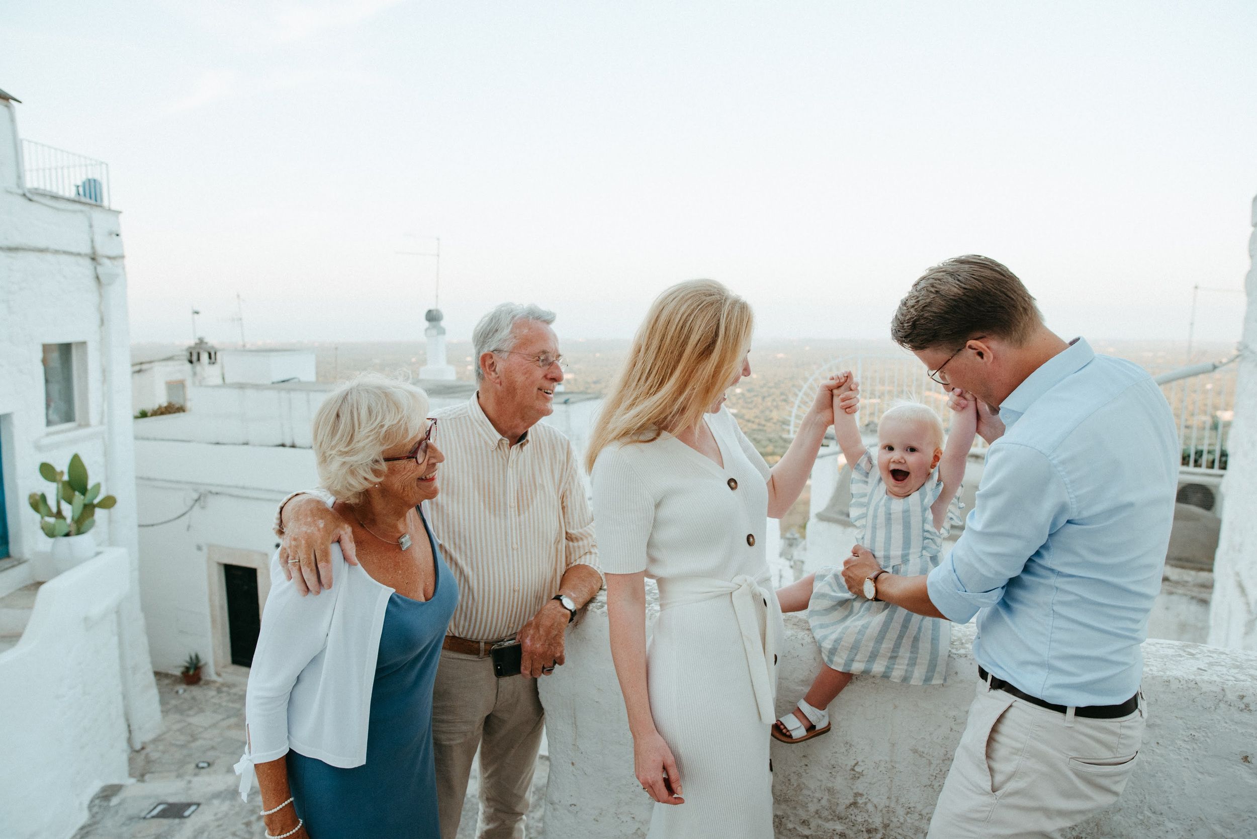 Group celebrates joyfully on white rooftop terrace with Mediterranean architecture.