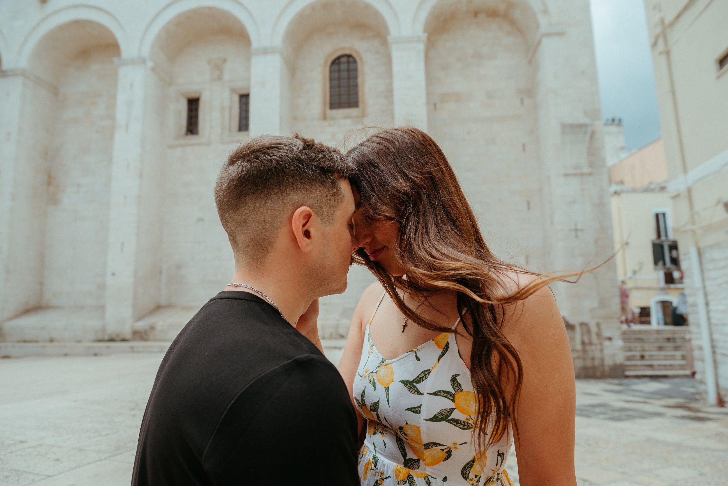 Couple sharing a tender moment in front of a white stone church with arched architecture.