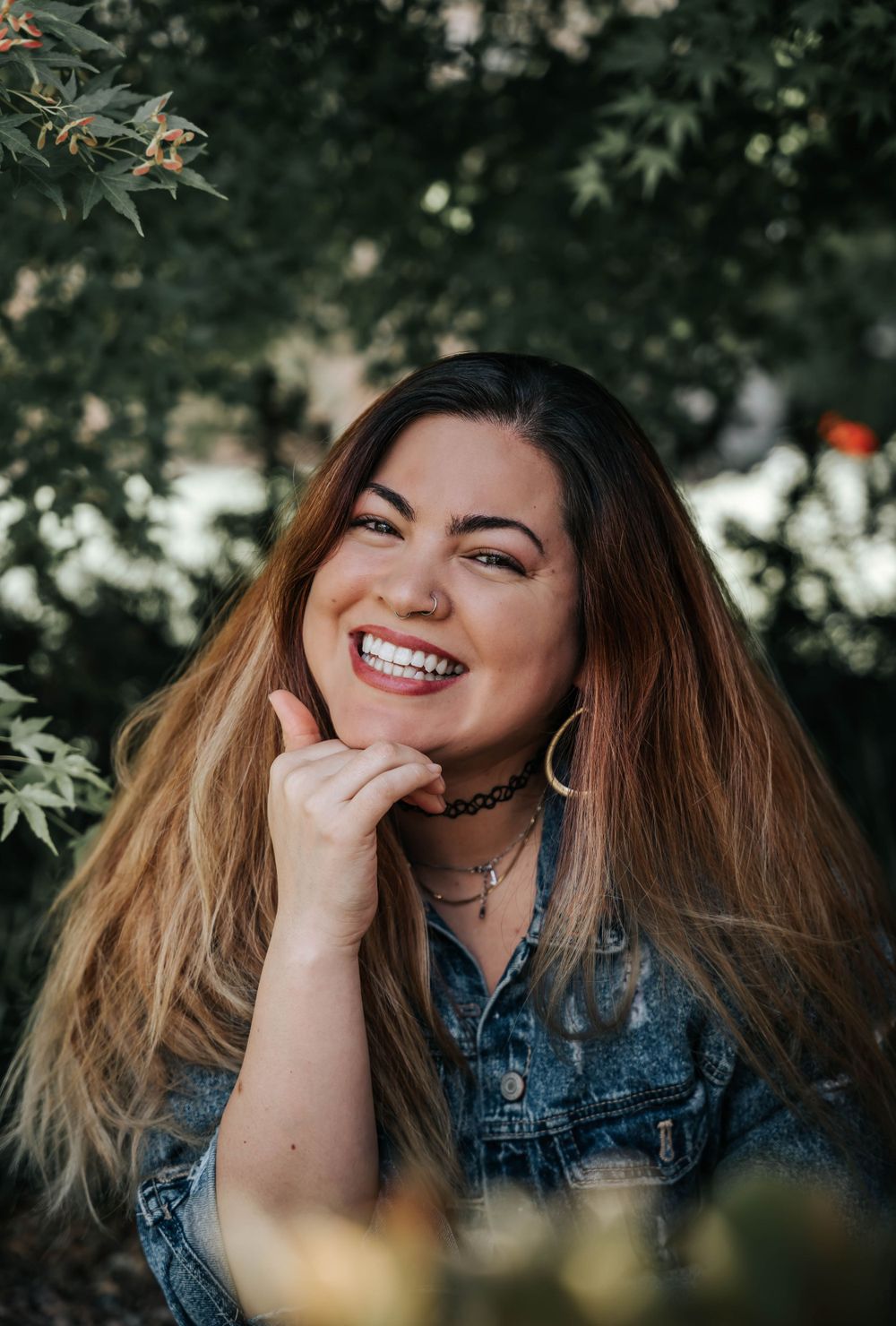 Close up portrait showing joyful expression and denim jacket with trees in soft focus background.