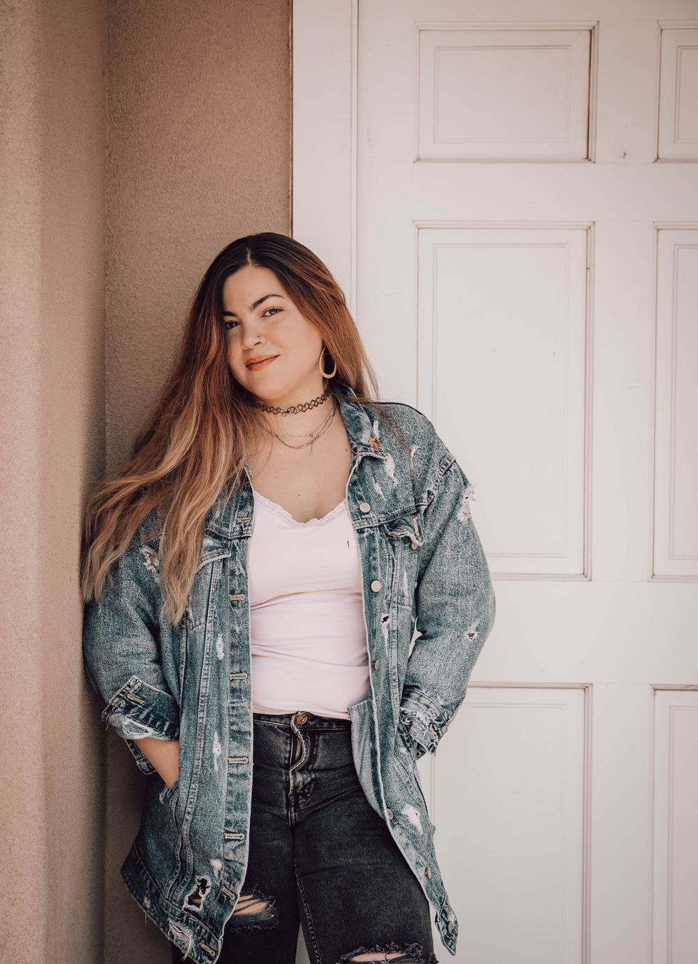 Stylish portrait featuring distressed denim jacket and choker necklace against white door background.
