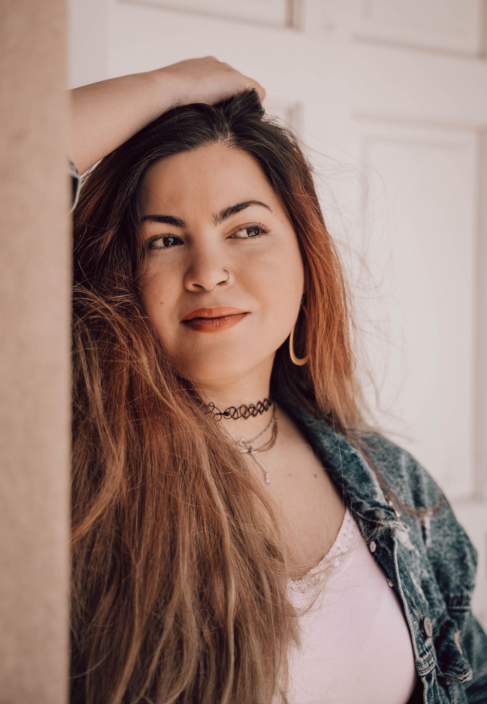 Indoor portrait series against light wall showing casual style with denim jacket and choker.