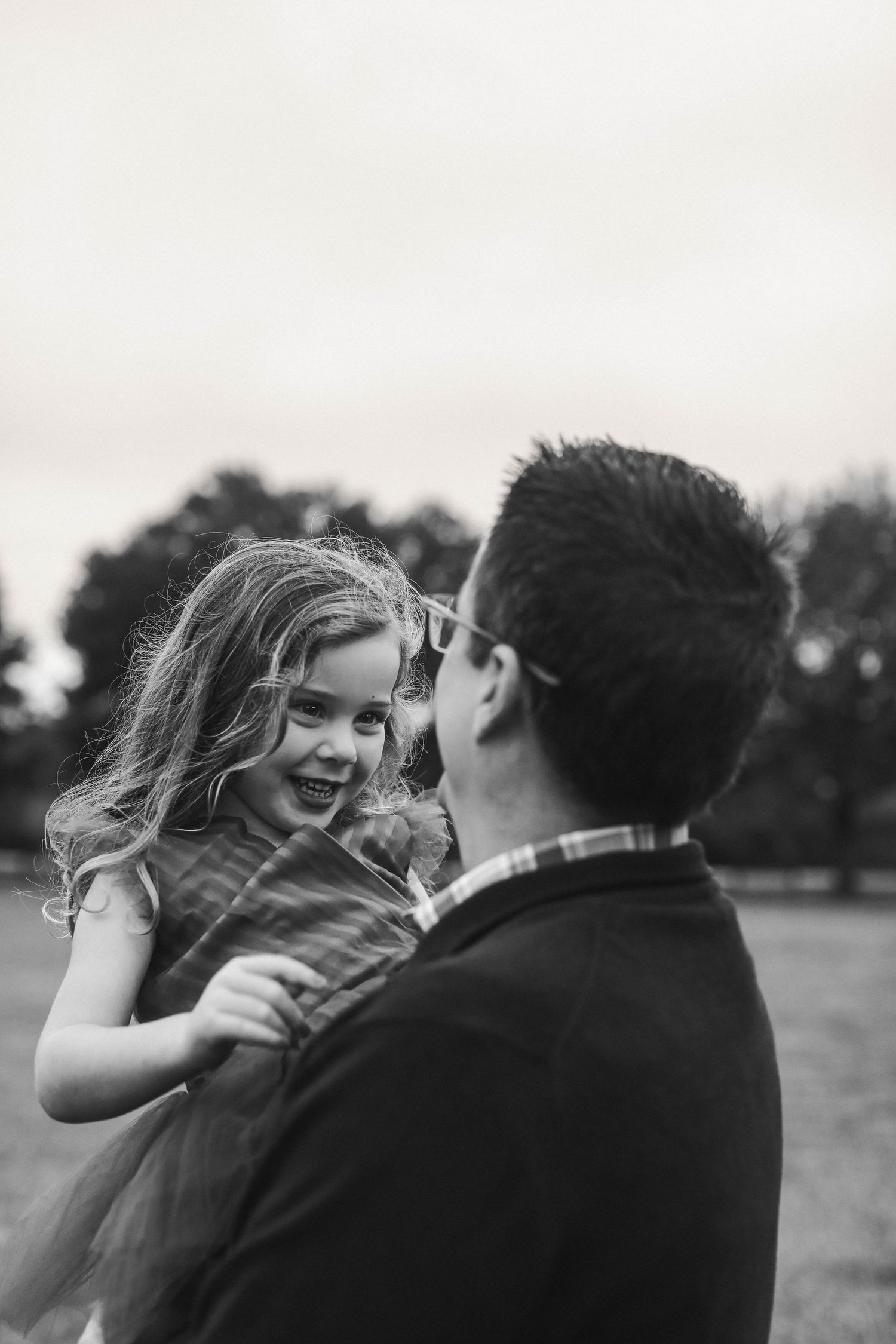 A candid black and white moment captured between a child and parent during a playful interaction outdoors.