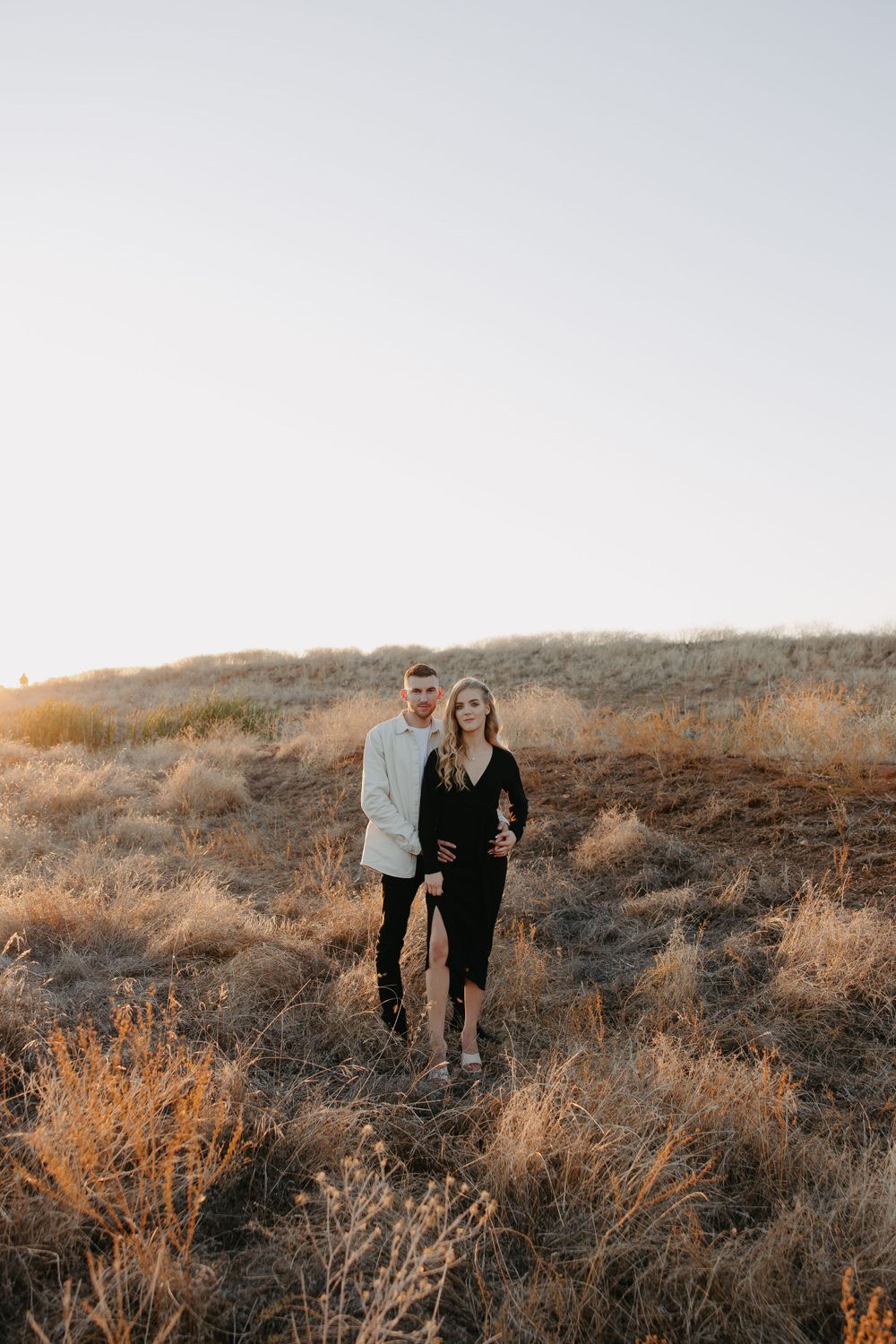 A couple in contrasting black and white outfits walking together on a rustic hillside trail.