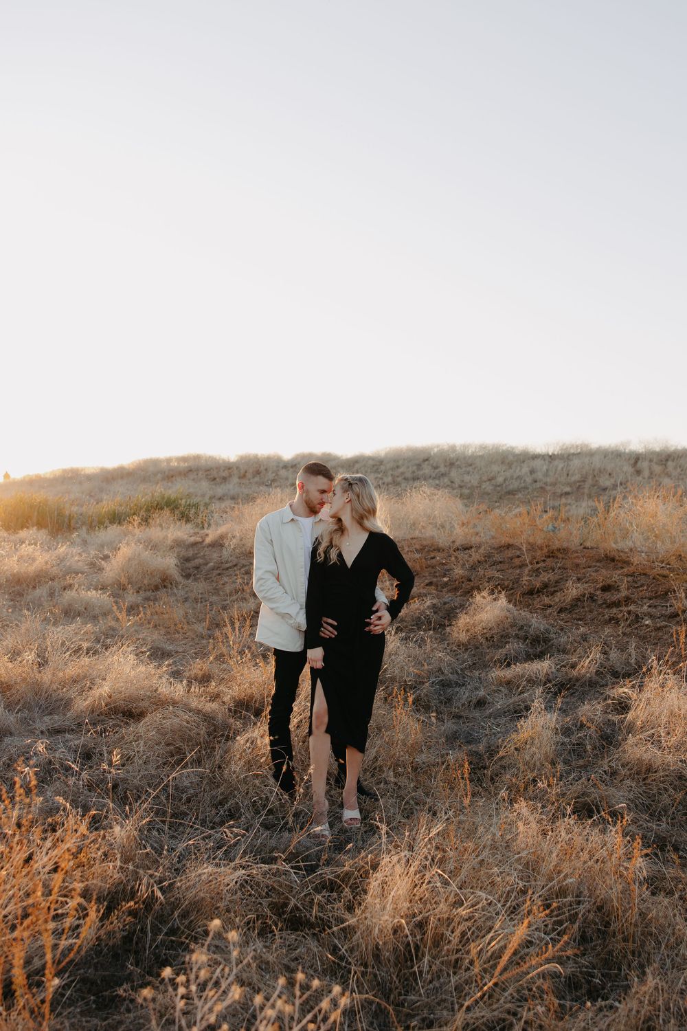 A stylish couple in contrasting outfits poses on a hill covered in golden brush.