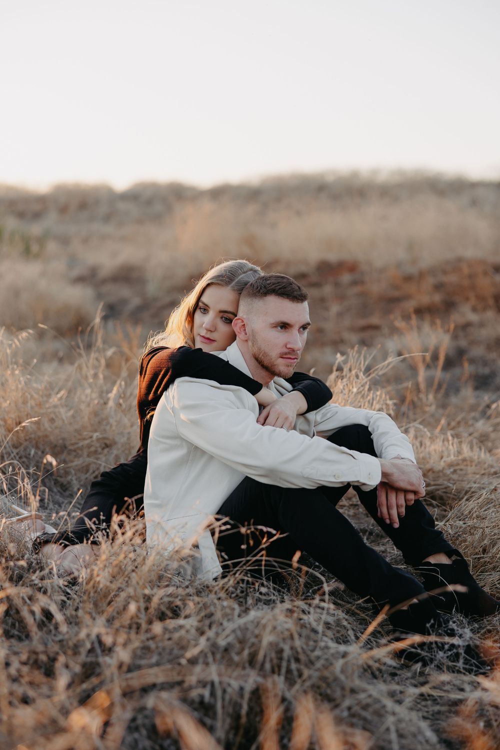 A couple shares an intimate moment while sitting on a hillside at sunset.