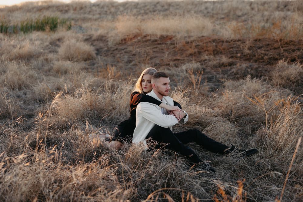 A couple sits back-to-back on a desert hillside during golden hour.