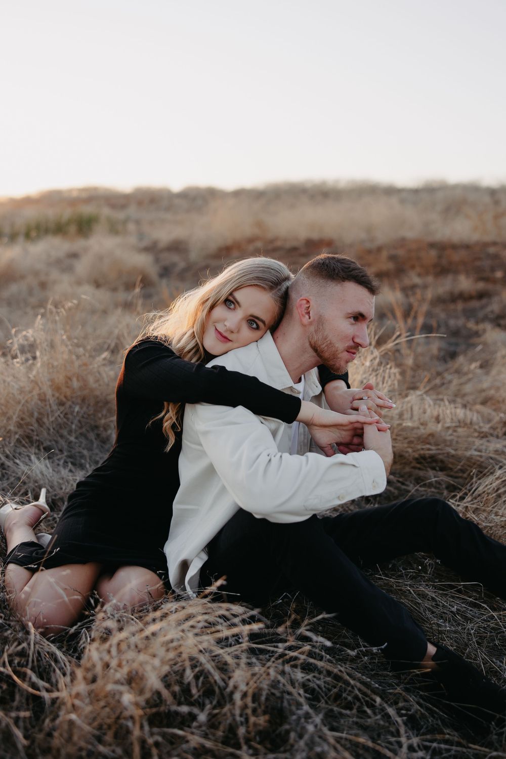 A joyful couple embraces while sitting amongst dried brush during sunset.
