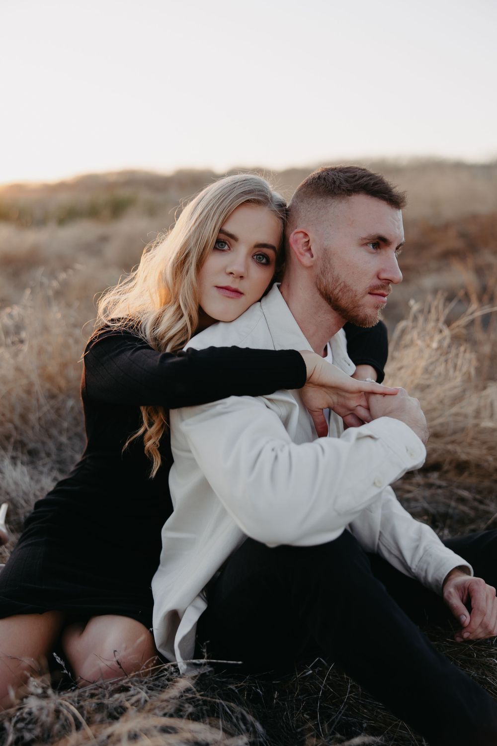 An intimate portrait of a couple sitting together in a brown grassy field.