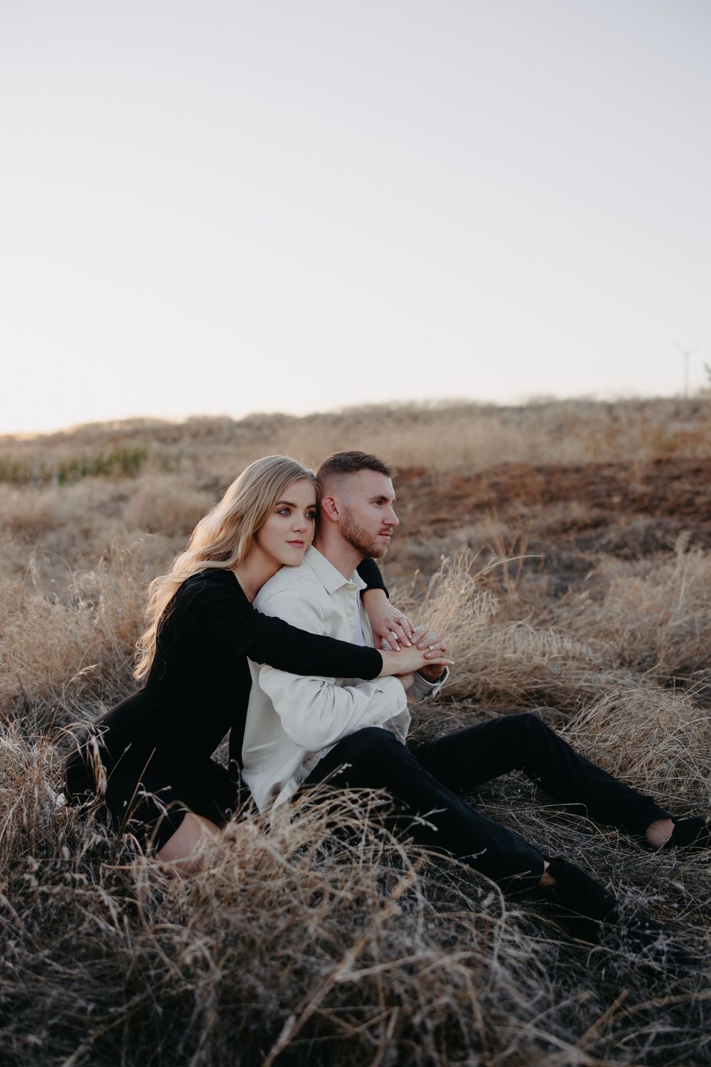A couple shares a tender moment while sitting in tall dried grass on a hillside.