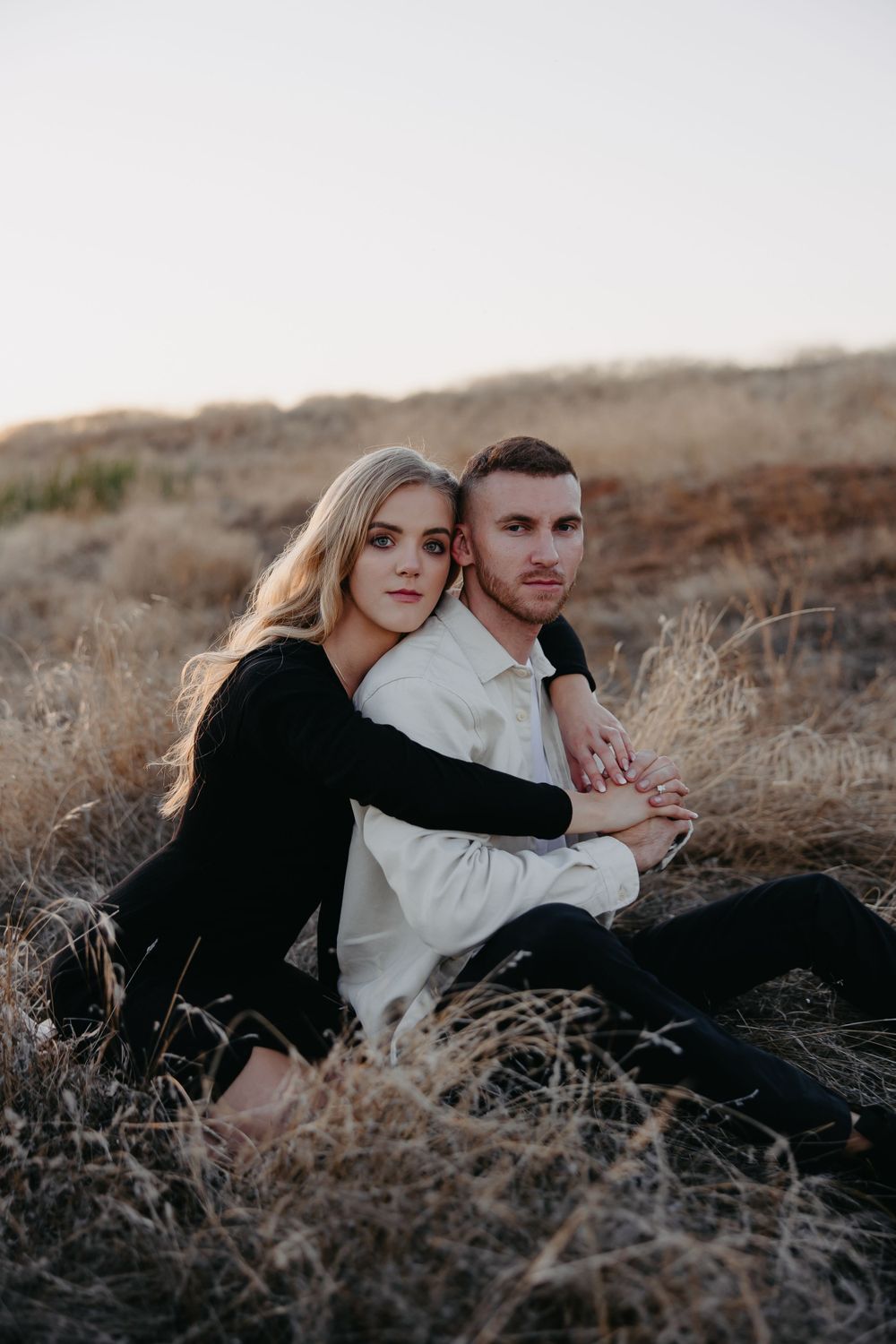 Couple poses for a romantic photoshoot among dried grass and hills.