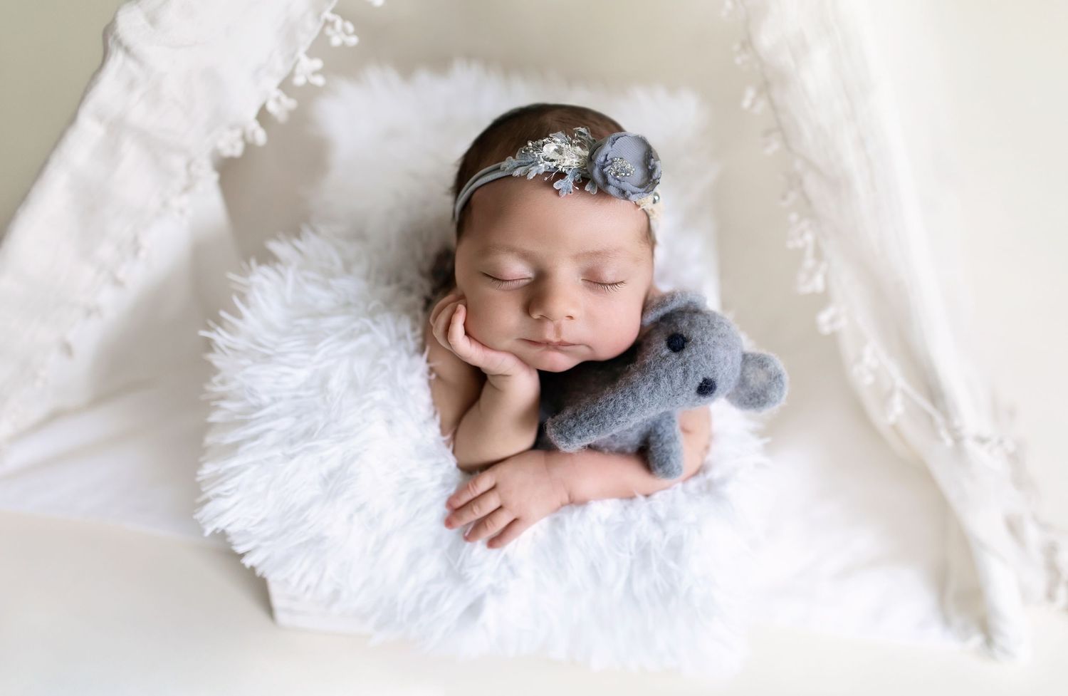 A newborn rests peacefully on soft white blankets in a series of artistic studio portraits.