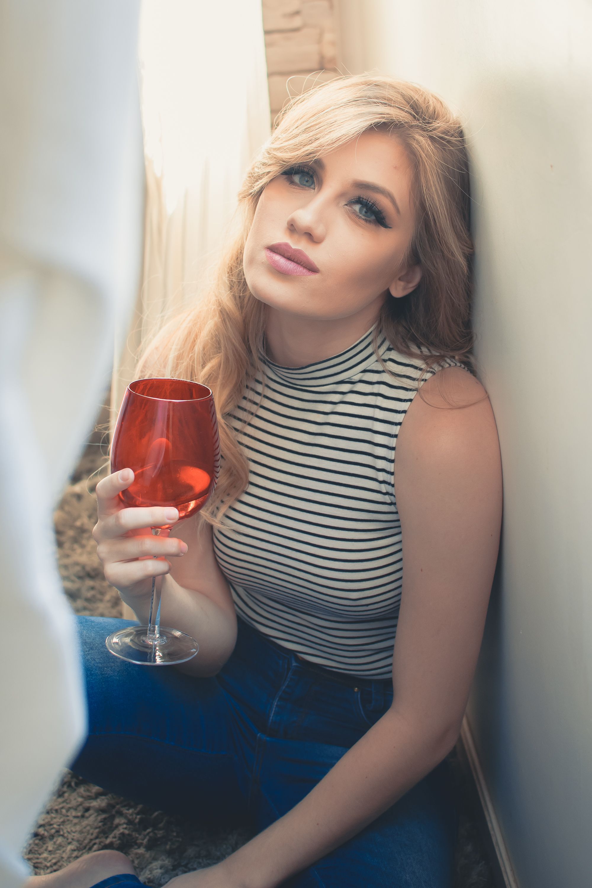 Figure in striped top holds wine glass while reclining in atmospheric lighting.