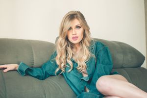 Casual portrait lounging on grey couch in teal dress with flowing blonde hair.