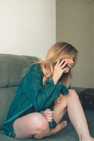 Candid moment on grey couch talking on phone wearing teal button-up dress.