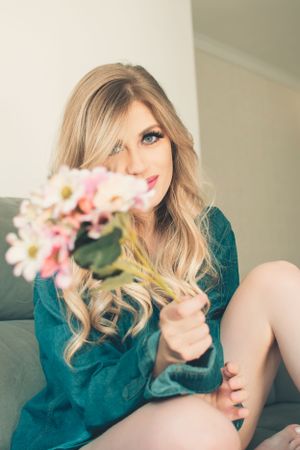 Romantic portrait on grey couch holding pink flowers in teal dress.