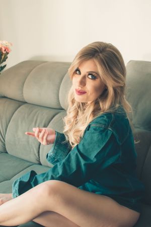 Fashion portrait on grey sofa in teal dress with styled blonde waves.
