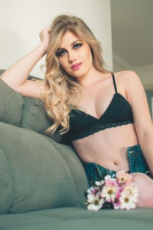 Romantic boudoir portrait on gray couch with flowers and teal denim styling.