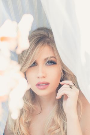 Dreamy portrait with soft lighting and floral elements against white curtains.