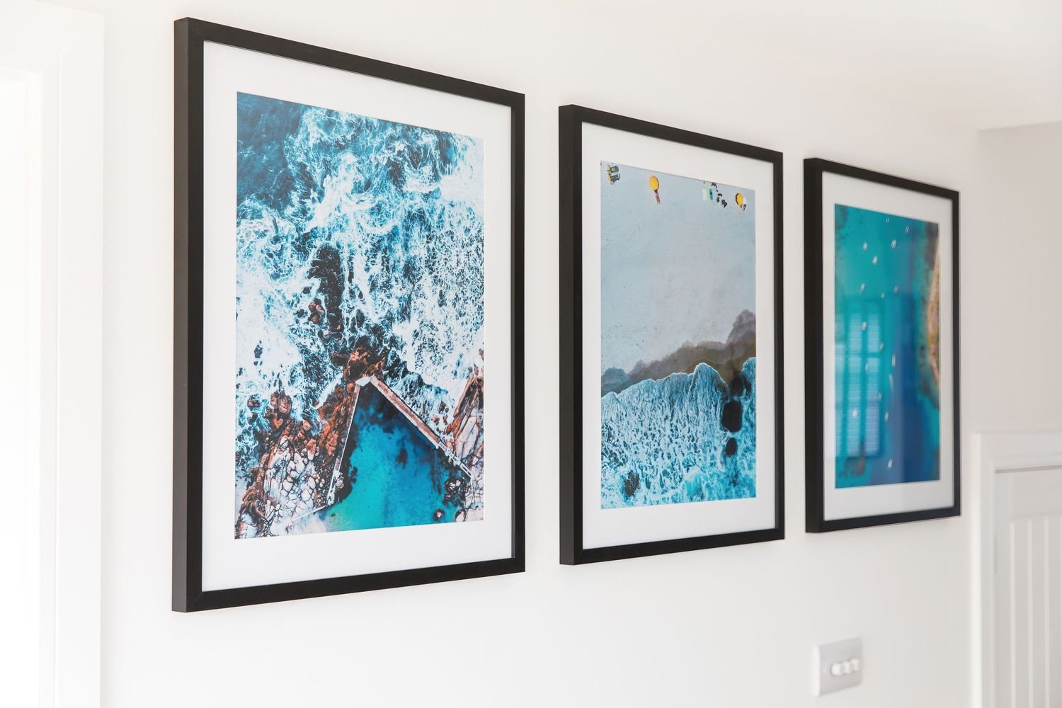 Series of framed aerial ocean photographs in blue tones displayed on white wall.