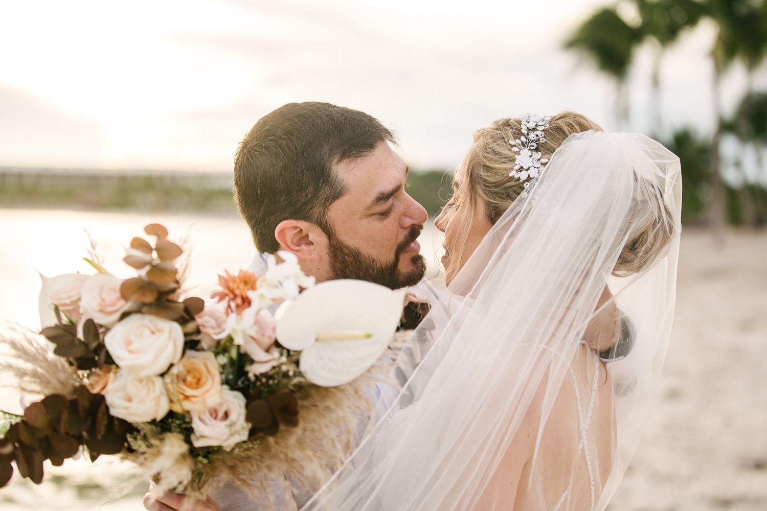 Romantic sunset beach wedding portrait with elegant floral bouquet.