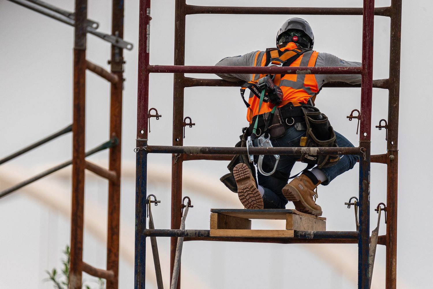 Construction worker in orange safety vest working on scaffolding structure.