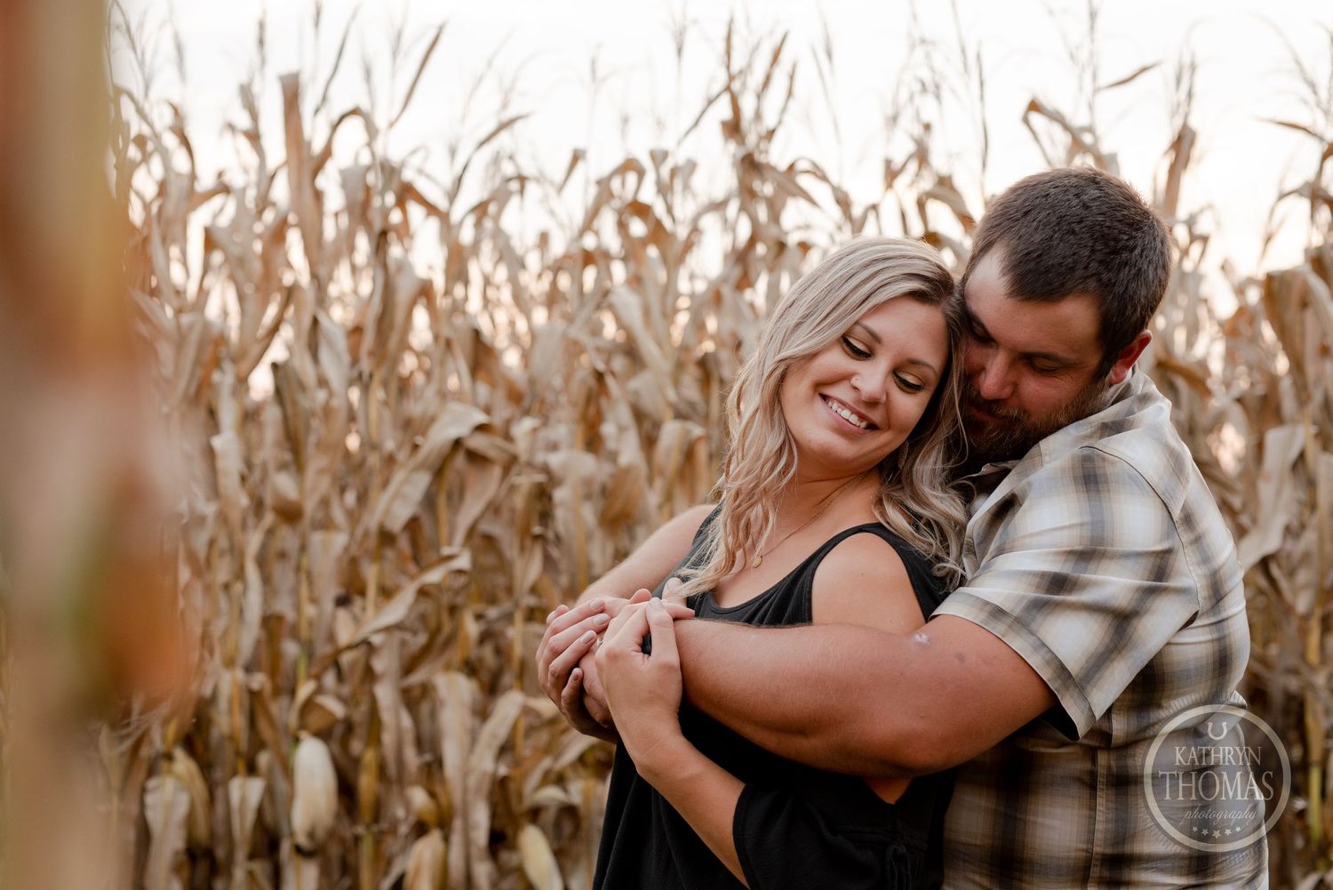 Couple embracing and laughing together in cornfield during golden hour.