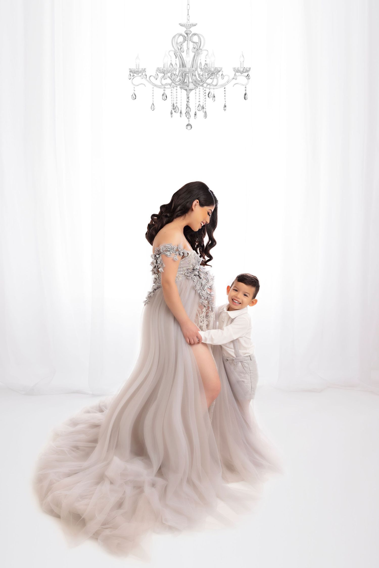 Ethereal maternity photo featuring a flowing gray dress with crystal embellishments under an ornate chandelier.