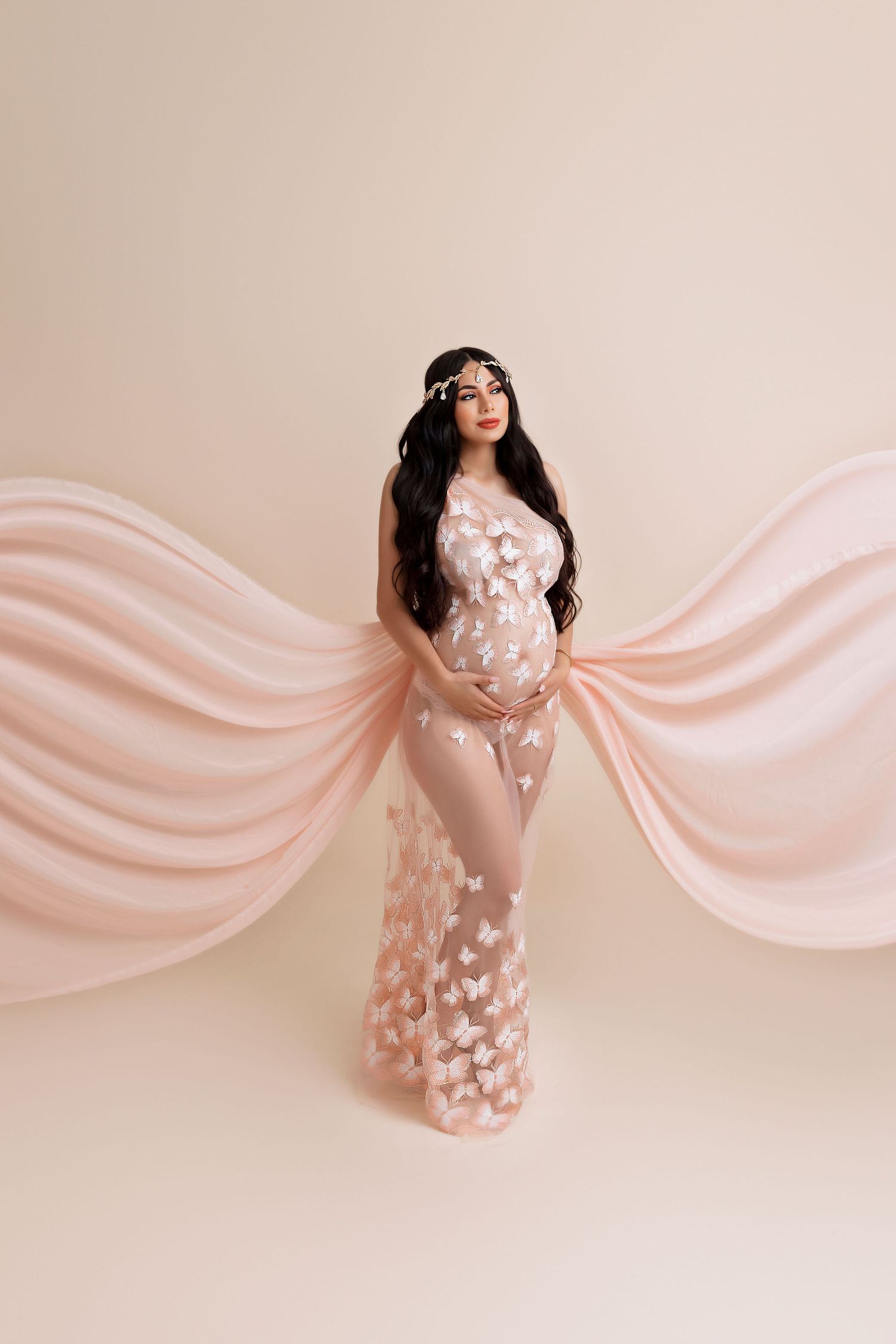 Artistic maternity portrait with flowing pink fabric and floral appliques against neutral background.