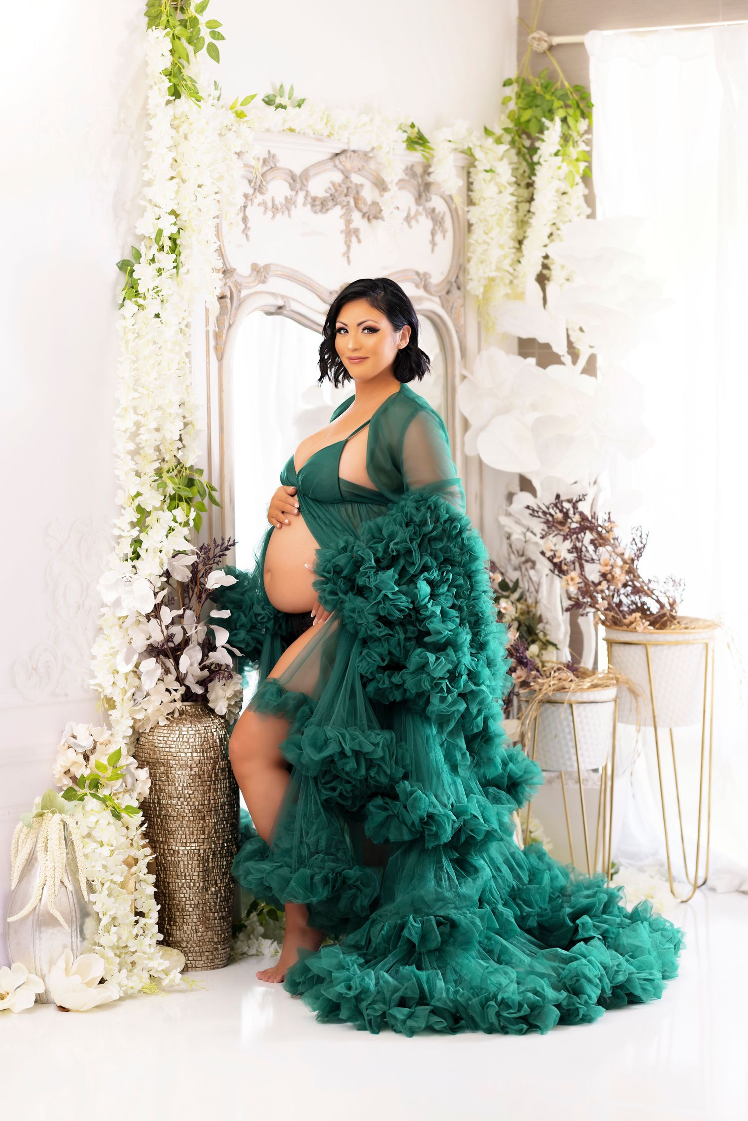 Dramatic maternity photo featuring emerald green tulle gown with floral and metallic decor.