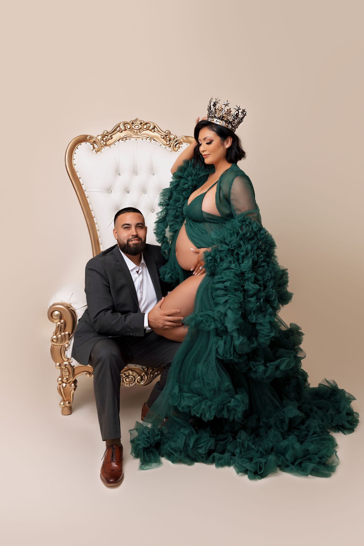 Elegant maternity portrait on ornate gold throne with emerald green tulle gown.