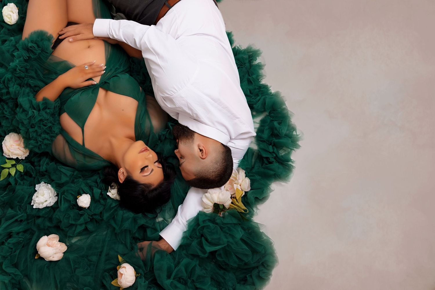 Overhead maternity photo with emerald green tulle fabric and white roses as props.