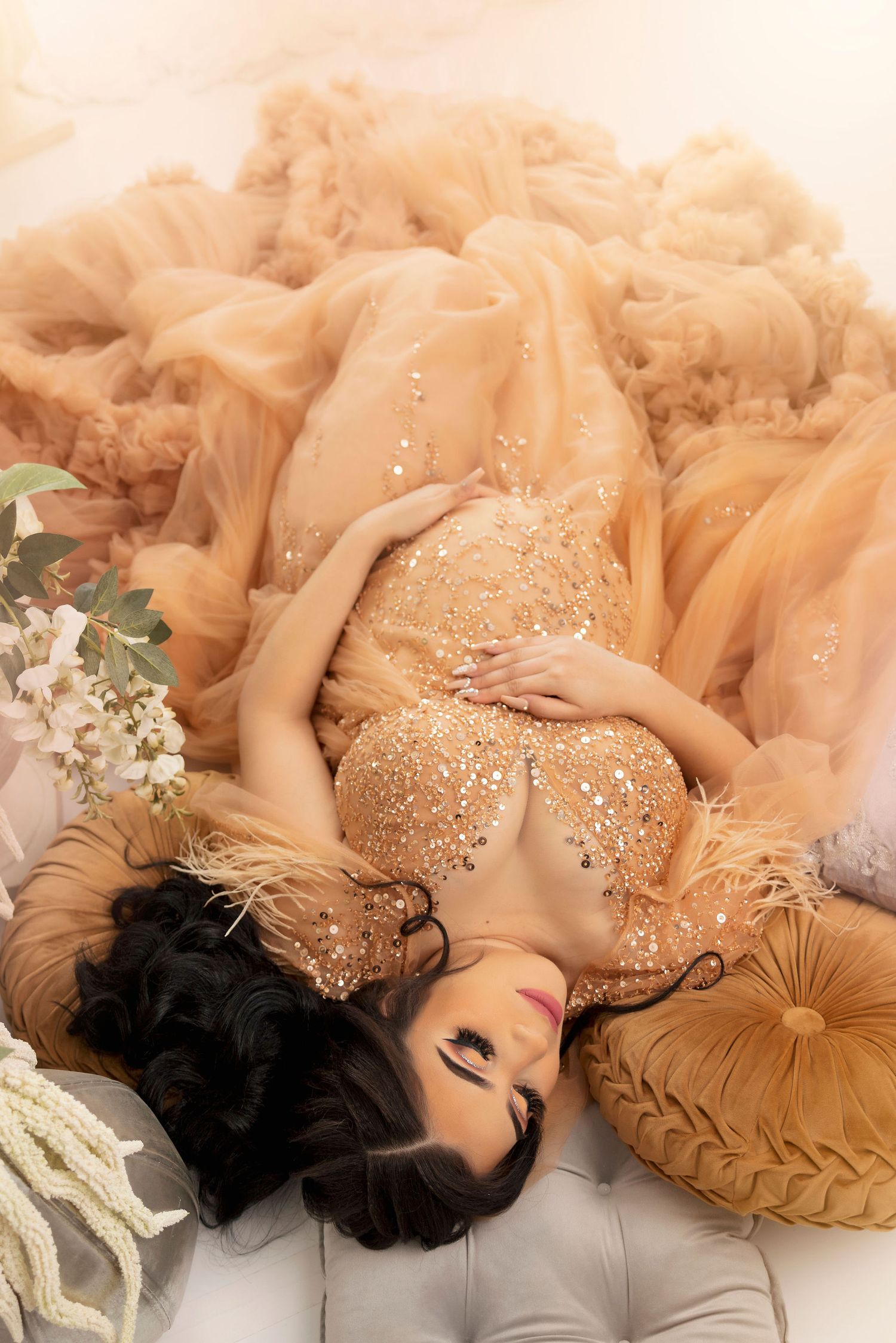 Glamorous maternity portrait in sparkly gold dress on tufted furniture.