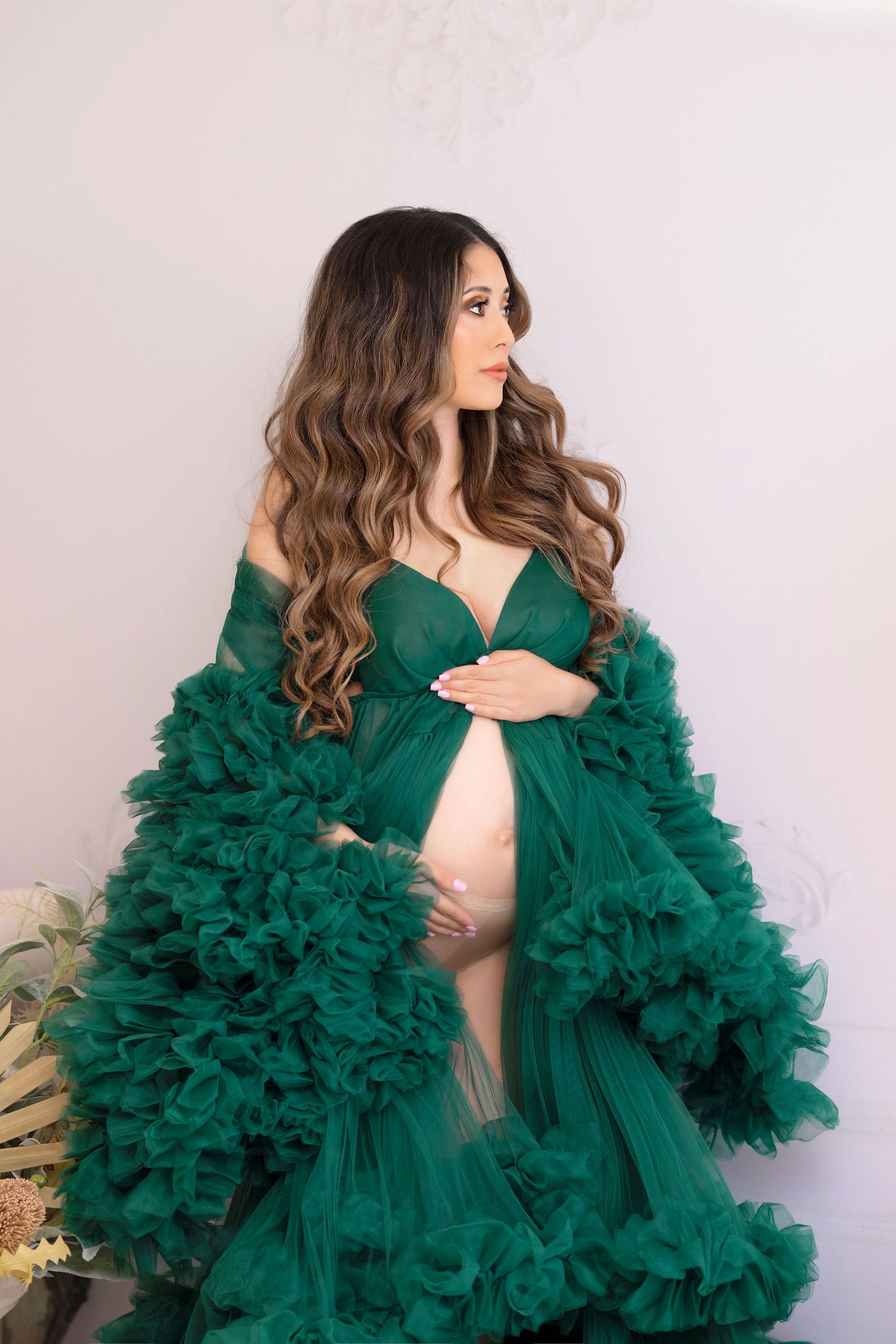 Maternity photo featuring emerald green tulle gown with ruffles against neutral background.