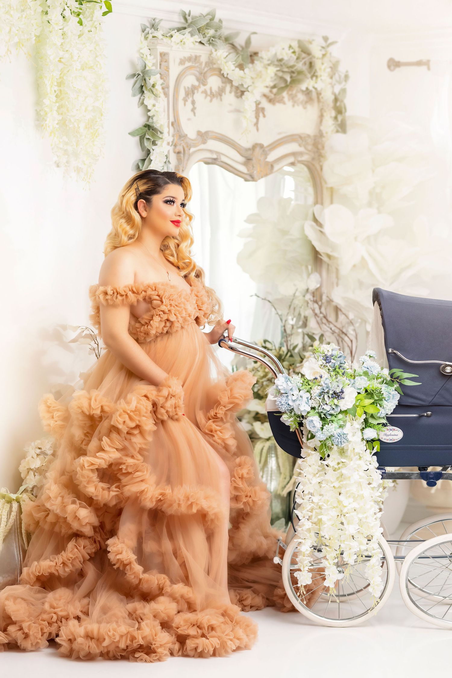 Maternity portrait featuring peach ruffled gown and vintage pram with floral arrangements.