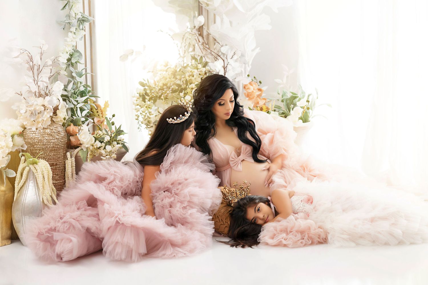 Dreamy maternity photo session with pink tulle gowns in an elegant white setting.