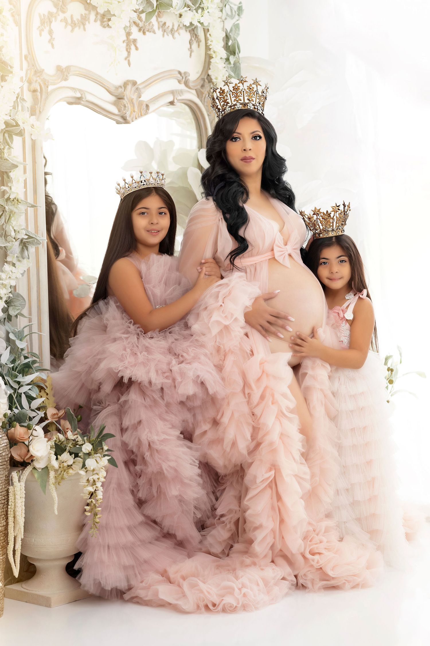 Elegant family portrait featuring matching pink tulle gowns and crowns in a floral setting.