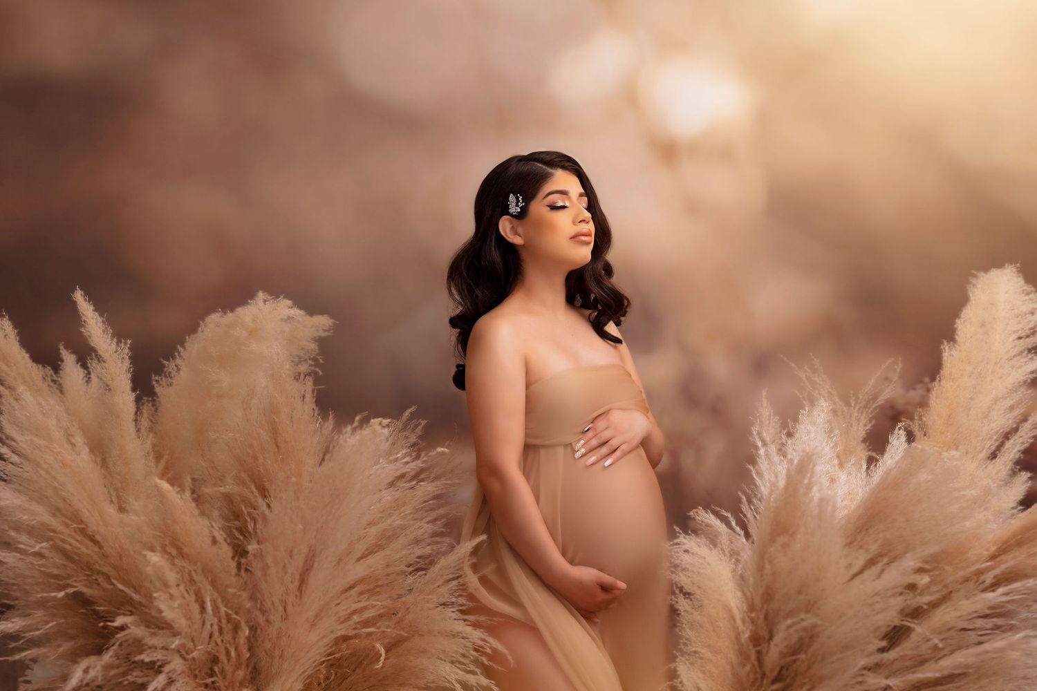Artistic maternity photo with pampas grass and natural light creating ethereal atmosphere.