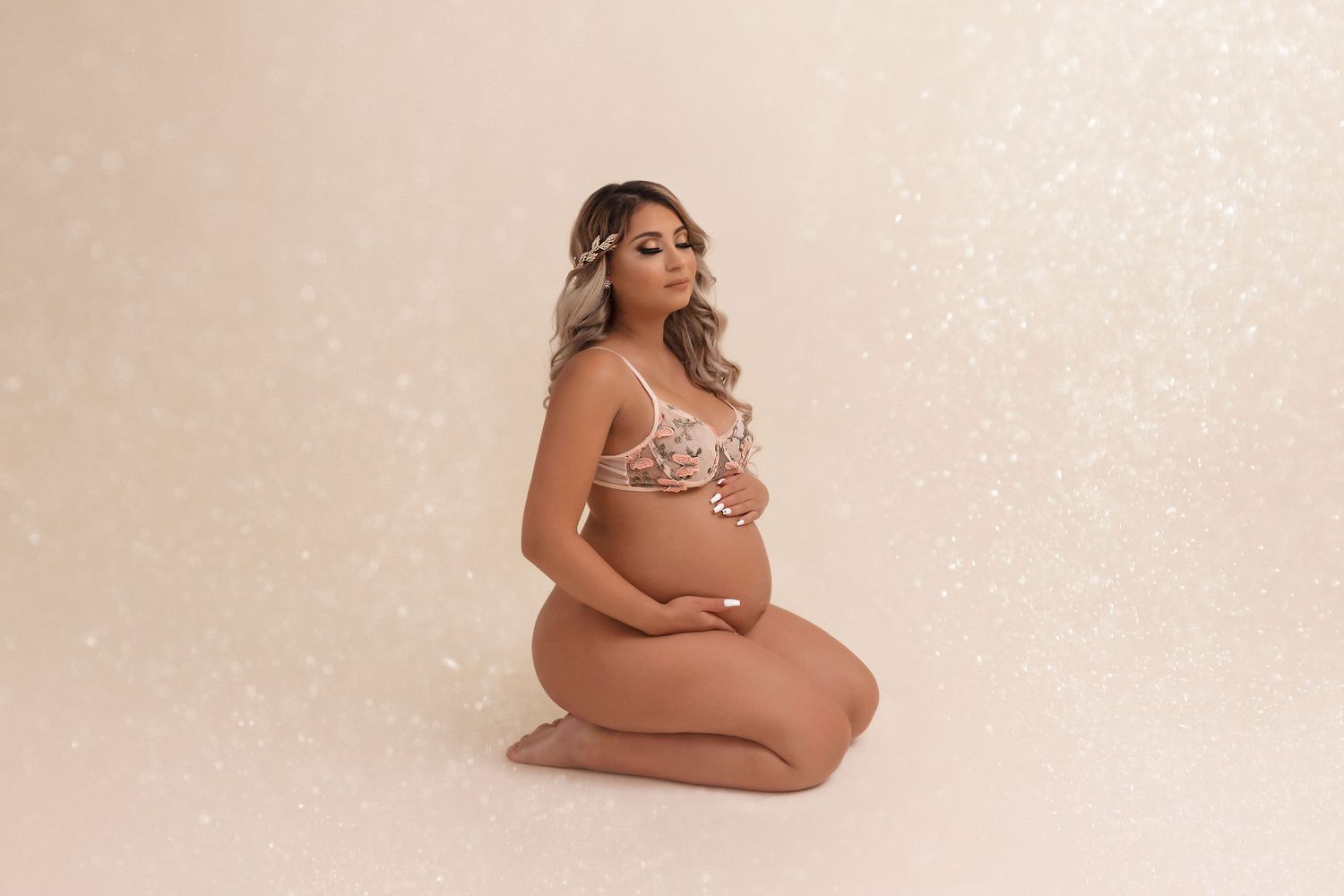 Maternity boudoir photo with lace lingerie against neutral beige backdrop.