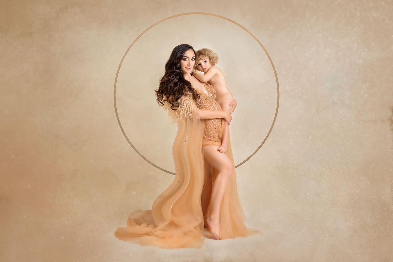 Artistic maternity portrait with flowing peach gown against gold circular backdrop.