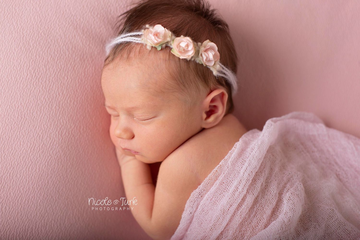 above close up of newborn baby girl in pink on her side with delicate rose headband