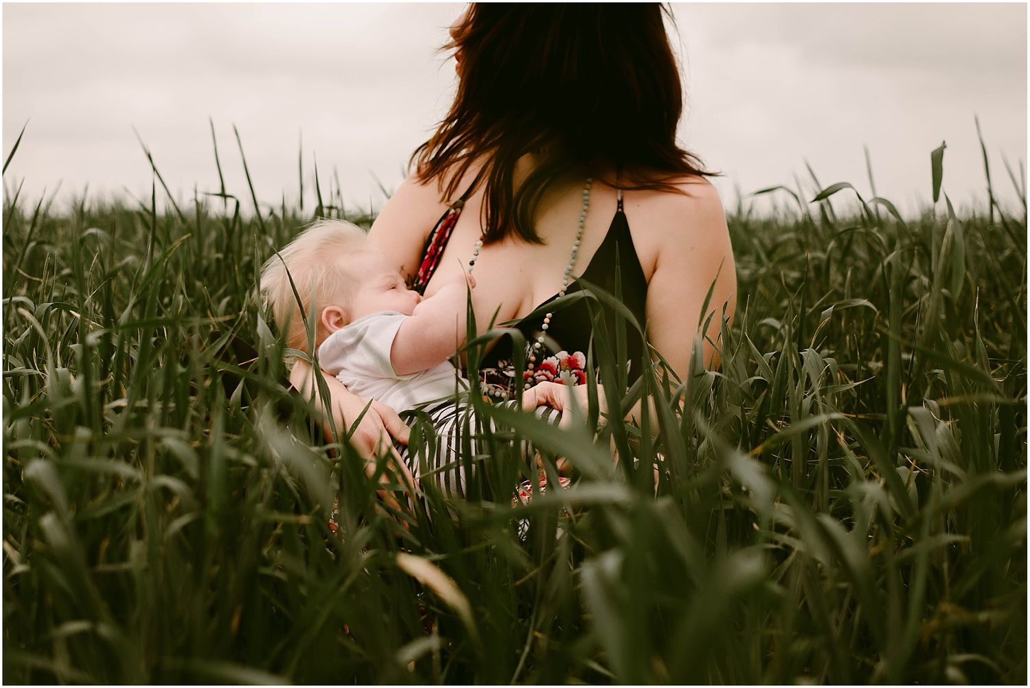 Tender moment photographed from behind in tall grassy field at sunset.