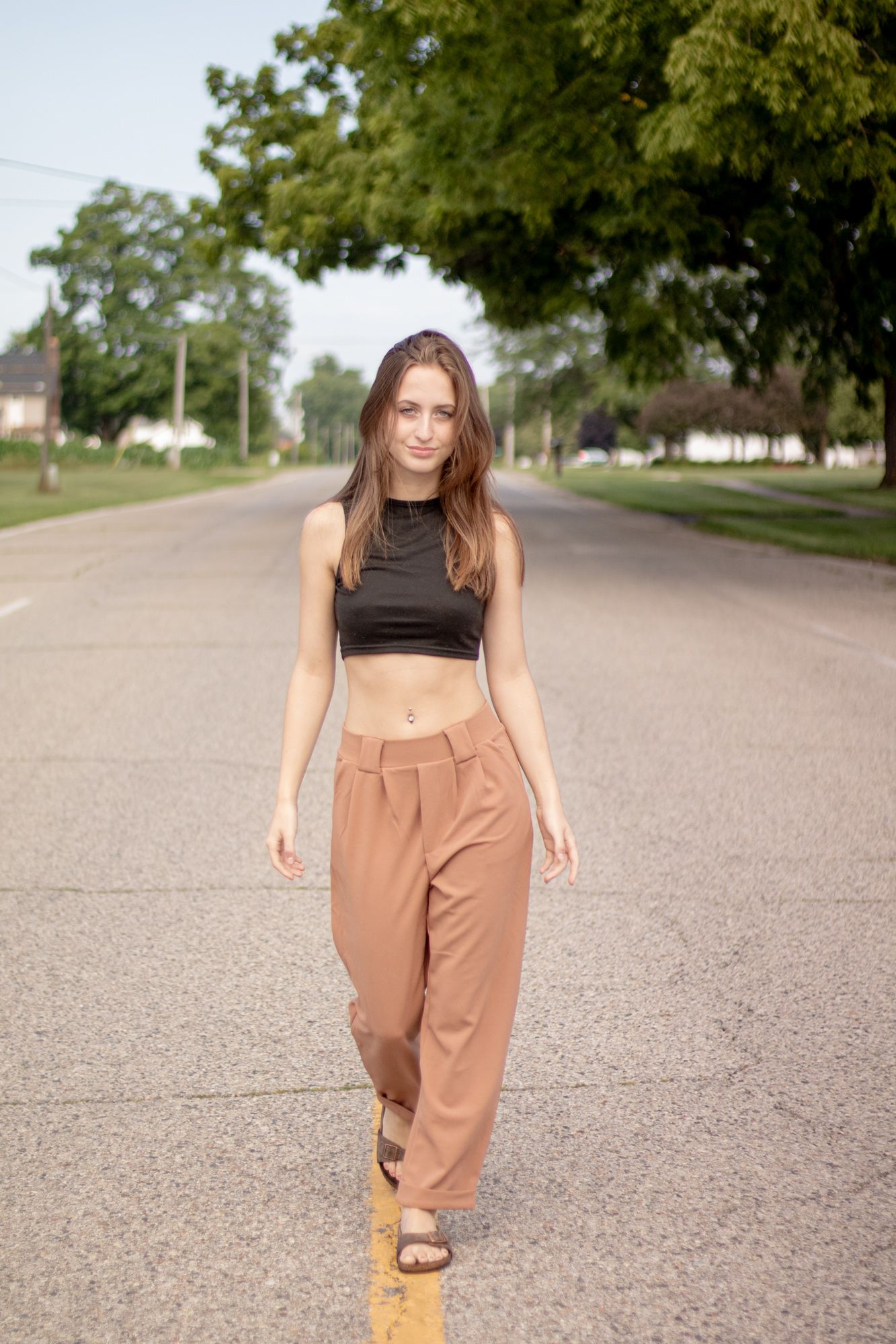 Stylish summer outfit featuring high-waisted tan pants and a black crop top on a sunny suburban street.