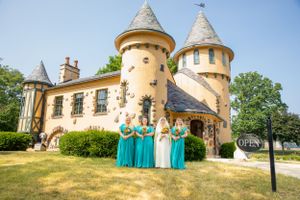 Bridesmaids in turquoise dresses pose in front of a fairy tale castle-style venue.