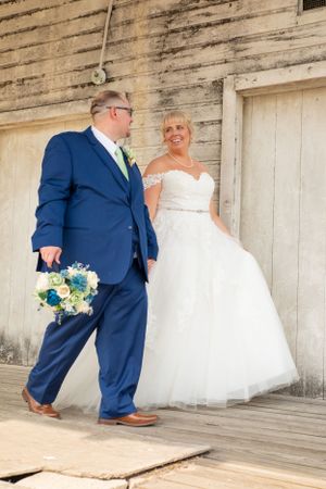 Wedding couple standing on wooden porch with bride in white ball gown and groom in navy suit.