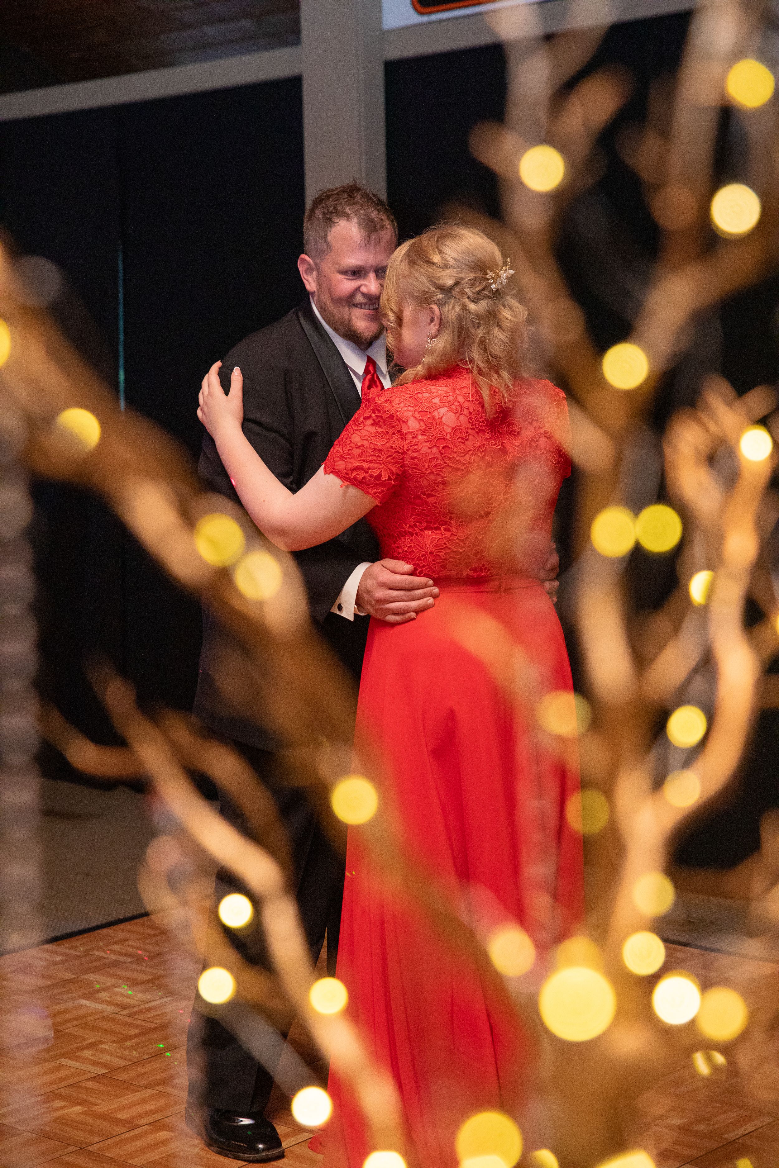 A couple shares an intimate dance at their wedding reception, with golden bokeh lights creating a romantic atmosphere.