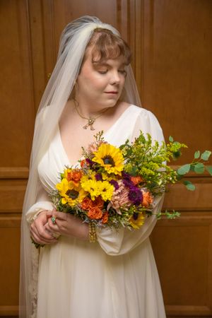 Bride in vintage-style dress holding vibrant sunflower and wildflower bouquet.