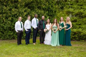 Wedding party poses outdoors with bridesmaids wearing different shades of green dresses.