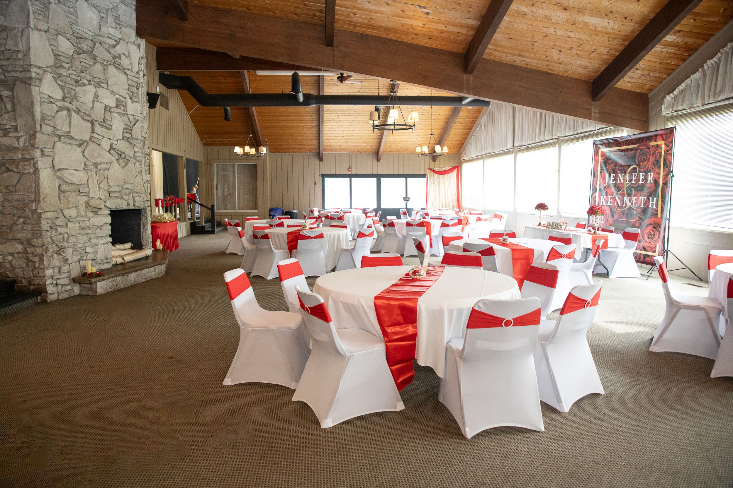A reception venue with white spandex chair covers and red table runners.